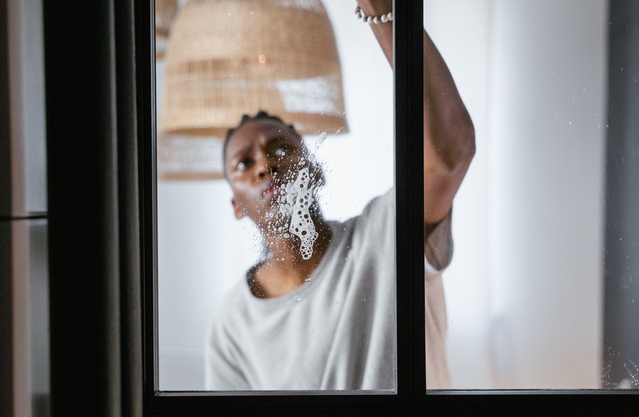 services-01 An adult male cleaning a glass window indoors, focusing on household chores and cleanliness.